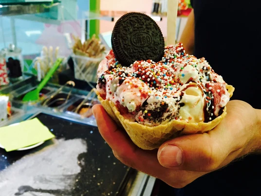 Eisdiele Schlecks in Osnabrück Ein Waffelbecher voller Eis mit bunten Streuseln und Oreo dekoriert, in einer Hand gehalten.