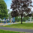 Freibadpark Lübbecke Spielplatz mit blauen Klettergeräten und Rutsche, daneben ein Baum und im Hintergrund ein Sprungturm.