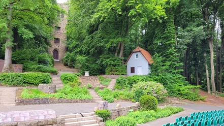 Freilichtbühne Nettelstedt Freilichtbühne umgeben von Wald, zwei steinerne Treppen führen zu einem historischen Turm und einem Häuschen.