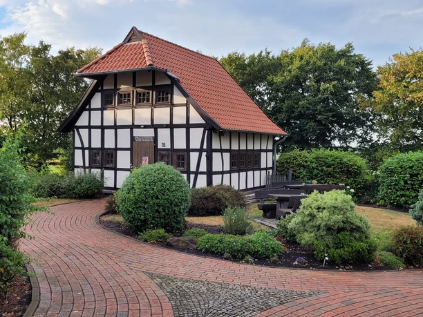 Eilhausen Backhaus Ein traditionelles Fachwerkgebäude mit roten Ziegeln umgeben von gepflegten, grünen Gartenanlagen.
