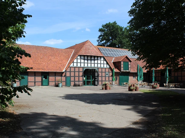 Half-timbered courtyard with green doors and windows in a rural setting under a blue sky.