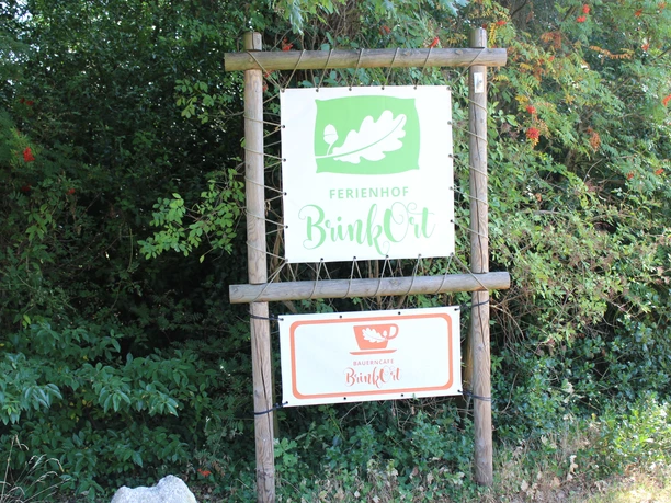 Entrance sign to Ferienhof BrinkOrt Warmsen, surrounded by lush green foliage.