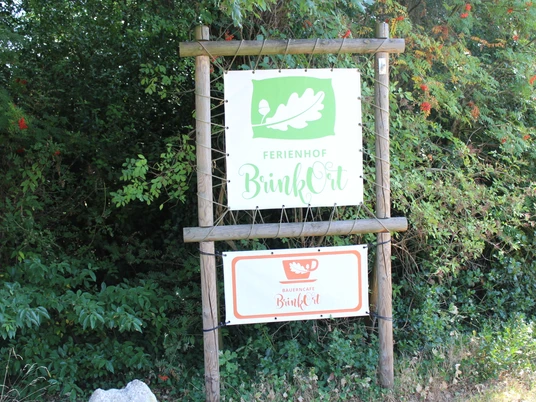 Ferienhof BrinkOrt, Warmsen Eingangsschild des Ferienhofs BrinkOrt Warmsen, umgeben von üppigem, grünem Blätterwerk.