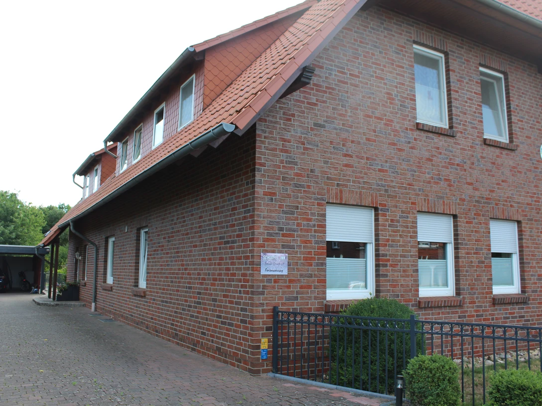 Schumi's Inn, Uchte Backsteinbau mit Satteldach im ländlichen Uchte, umgeben von Bäumen und gepflastertem Außenbereich.