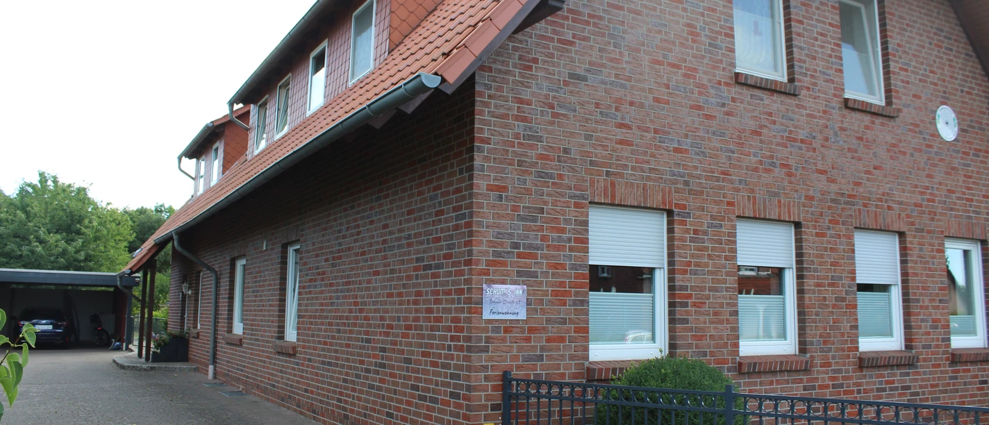 Schumi's Inn, Uchte Backsteinbau mit Satteldach im ländlichen Uchte, umgeben von Bäumen und gepflastertem Außenbereich.