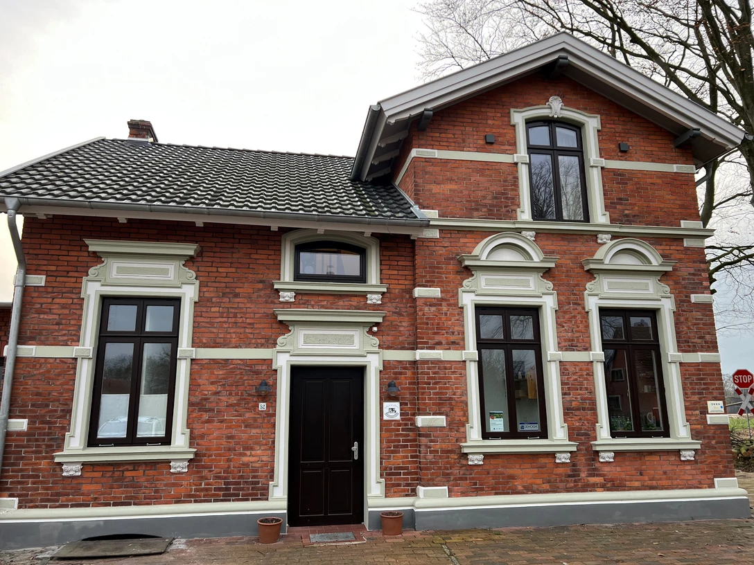 Historische rote Backsteinvilla mit weißen Fensterrahmen und hölzernen Türen, umgeben von Bäumen.