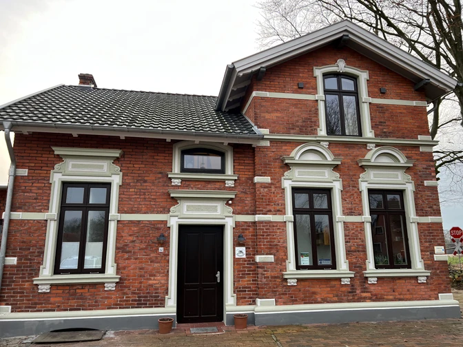 Historische rote Backsteinvilla mit weißen Fensterrahmen und hölzernen Türen, umgeben von Bäumen.