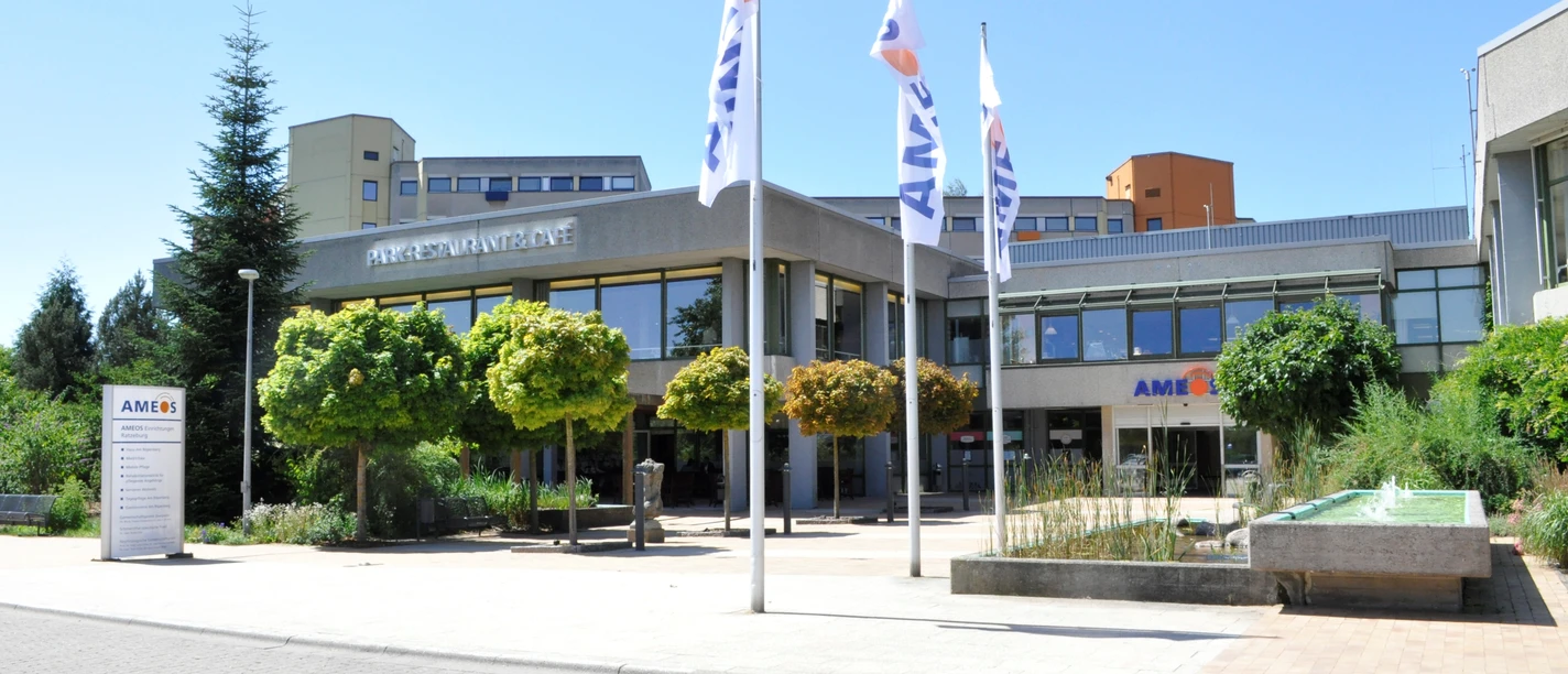 AMEOS_Eingang (©AMEOS Einrichtungen Ratzeburg).jpg Die Senioreneinrichtung von außen. Vor dem Eingang stehen Bäume und gehisste Fahnen mit der Aufschrift AMEOS