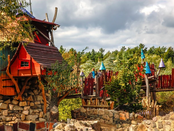Felsennest Ein märchenhaftes Baumhaus-Gebilde mit Brücke aus Holz und farbenfrohen hexenhutartigen Dekorationen.