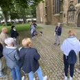 Eine Gruppe von Menschen lauscht aufmerksam einem Stadtführer vor einer historischen Kirche in Lübbecke.