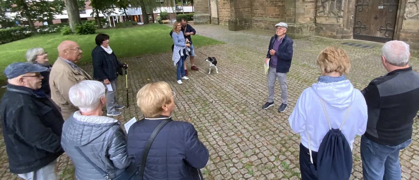 Eine Gruppe von Menschen lauscht aufmerksam einem Stadtführer vor einer historischen Kirche in Lübbecke.