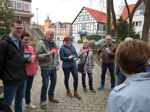 Lübbecke_Stadtführung_Echt oder Ente3_Oliver Krato.jpg Eine Gruppe von Menschen steht lächelnd im Freien und hält Schilder mit "Echt" oder "Ente".