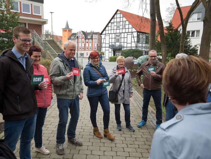 Lübbecke_Stadtführung_Echt oder Ente3_Oliver Krato.jpg Eine Gruppe von Menschen steht lächelnd im Freien und hält Schilder mit "Echt" oder "Ente".