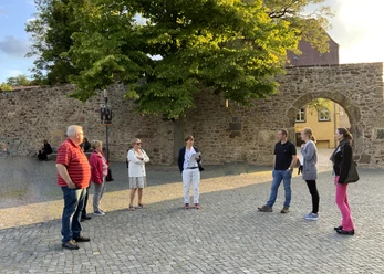 Stadtführungen in Lübbecke_2.jpg Eine Gruppe von Menschen steht auf einem gepflasterten Platz vor einer historischen Steinmauer.