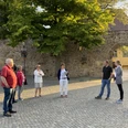 Stadtführungen in Lübbecke_2.jpg Eine Gruppe von Menschen steht auf einem gepflasterten Platz vor einer historischen Steinmauer.
