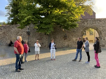 Stadtführungen in Lübbecke_2.jpg Eine Gruppe von Menschen steht auf einem gepflasterten Platz vor einer historischen Steinmauer.