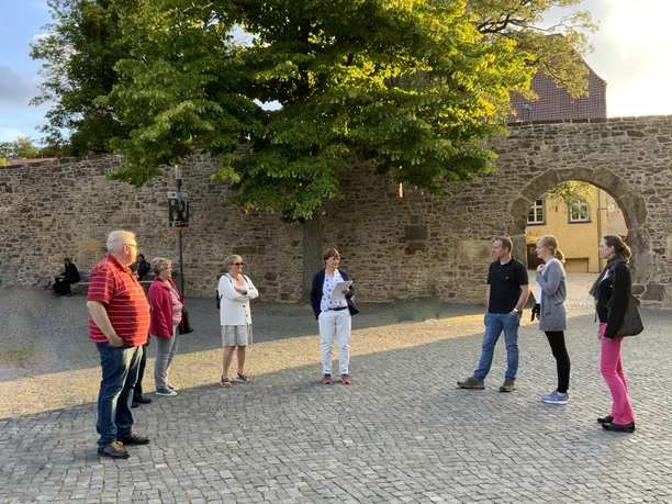 Stadtführungen in Lübbecke_2.jpg Eine Gruppe von Menschen steht auf einem gepflasterten Platz vor einer historischen Steinmauer.