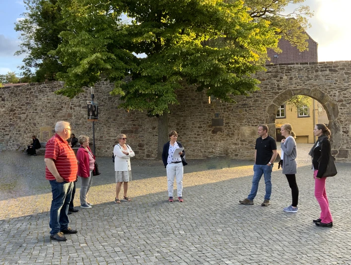 Stadtführungen in Lübbecke_2.jpg Eine Gruppe von Menschen steht auf einem gepflasterten Platz vor einer historischen Steinmauer.