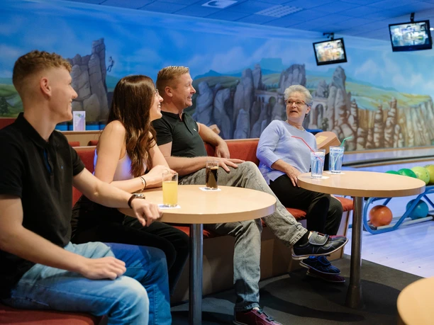 Bowling Vier Personen, die an einem Tisch in einer Bowlingbahn Getränke genießen.