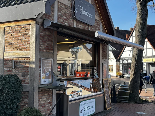 Aalräucherei Hodann Verkauf.jpeg Ein kleines Fachwerkgebäude beherbergt eine Aalräucherei mit Verkaufstheke unter blauem Himmel.