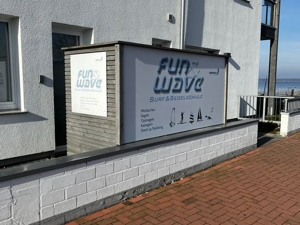 Fun and Wave Logo Ein modernes Gebäude mit einem großen Werbeschild der Fun & Wave Surf- und Segelschule.