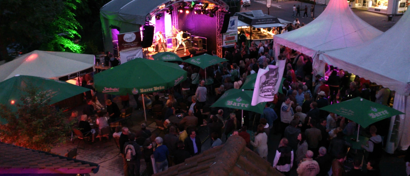 2013.jpg Menschen genießen ein abendliches Open-Air-Konzert unter lila Beleuchtung auf einem gut besuchten Platz.