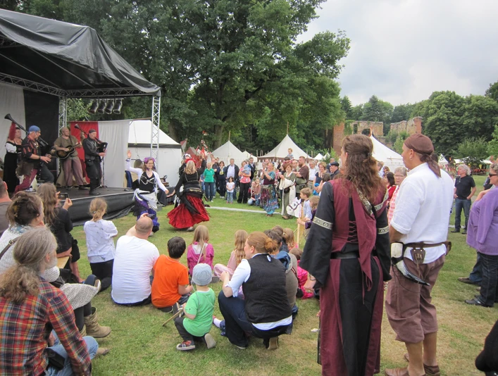 Mittelaterlicher Markt Besucher in mittelalterlicher Kleidung genießen Vorführungen vor einer Bühne auf einem belebten Markt.