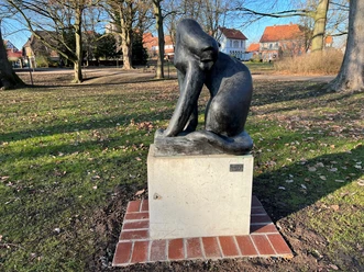 A bronze sculpture of a big cat on a pedestal in a park-like setting, surrounded by trees.