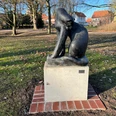 Raubkatze Bronzeskulptur einer Raubkatze auf einem Sockel in einem parkähnlichen Gelände, umgeben von Bäumen.