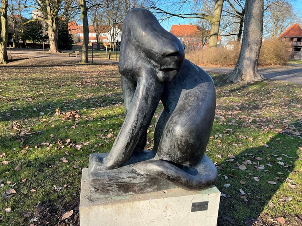 Raubkatze Bronzestatue einer sitzenden Raubkatze im Park, von kahlen Bäumen umgeben, auf einem Betonsockel.