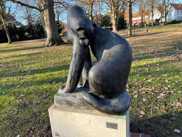 Bronzestatue einer Raubkatze mit nachdenklicher Haltung auf einem steinernen Sockel im Park.
