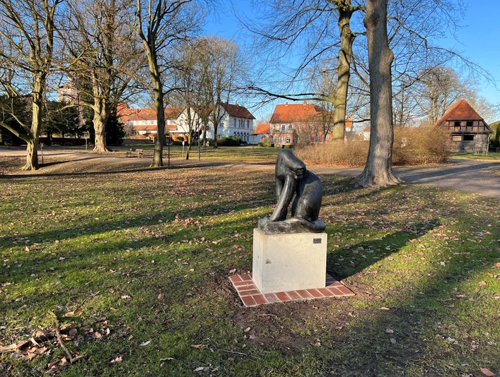 Raubkatze Skulptur einer stilisierten Raubkatze auf einem Sockel in einem sonnigen Park mit alten Gebäuden.