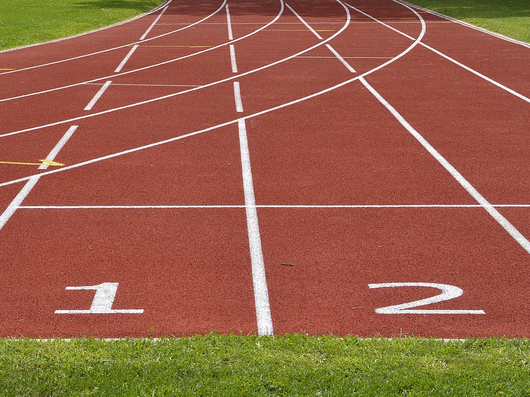 Rote Tartanbahn mit weißen Linien und Startnummern 1 und 2 auf einem grünen Sportfeld.