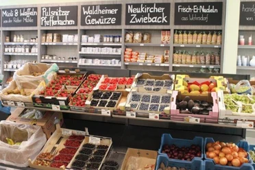Fruit- en groentekraam in een winkel met aardbeien, bosbessen, avocado's en druiven; op de achtergrond rekken met kruiden en pasta.