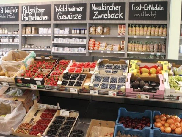 Fruit and vegetable stall in a store with strawberries, blueberries, avocados and grapes; in the background shelves with spices and pasta.