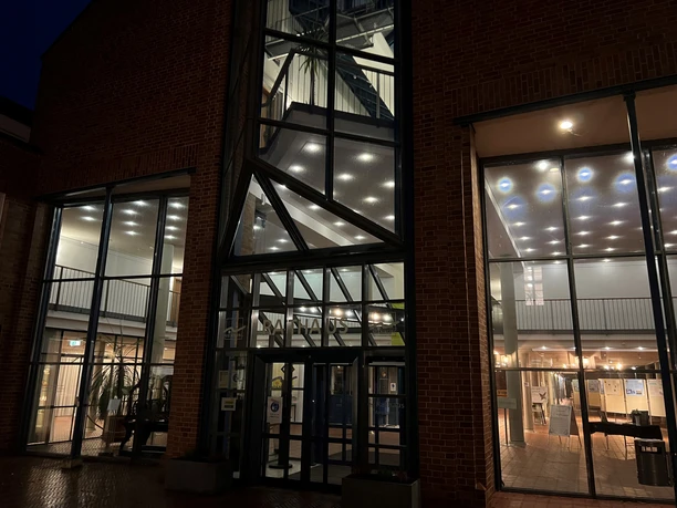 Rathaus Moderne Backsteinarchitektur am Abend, mit beleuchtetem Treppenhaus und großen Glasfronten.
