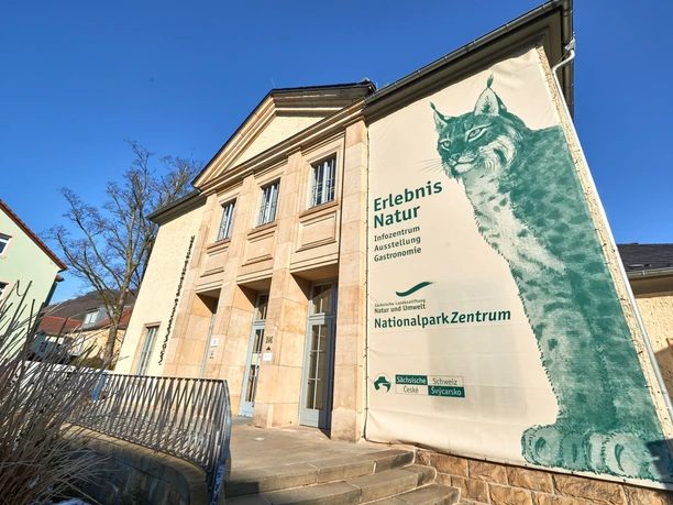 Nationalparkzentrum in Bad Schandau Eingangsbereich eines Gebäudes mit großem Plakat eines Luchses, das für das Nationalparkzentrum wirbt; blauer Himmel im Hintergrund.