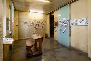 NS Dokumentationszentrum Ein heller Raum im NS-Dokumentationszentrum Köln. Historische Fotos schmücken blassgelbe Wände und eine Holzbank mit Pult bietet Platz zum Verweilen.