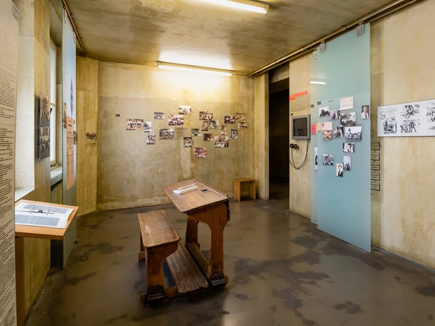 NS Dokumentationszentrum Ein heller Raum im NS-Dokumentationszentrum Köln. Historische Fotos schmücken blassgelbe Wände und eine Holzbank mit Pult bietet Platz zum Verweilen.