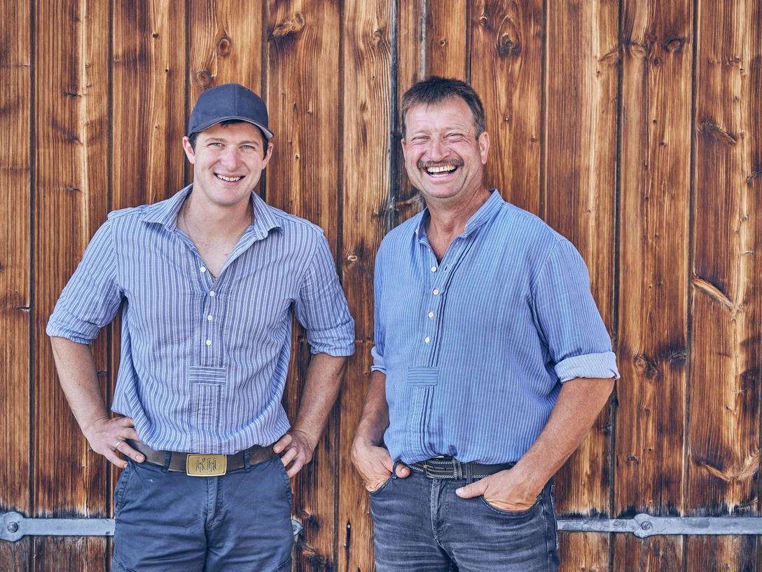Riegseer Weideochs_Spitzenprodukt Zugspitz Region_marcgilsdorf.jpg Zwei lächelnde Männer in blauen Hemden vor einer Holzvertäfelung.