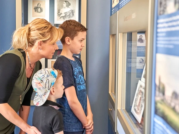 Ausstellung in den Richard Wagner Stätten in Graupa Eine Frau und zwei Jungen betrachten interessiert eine Ausstellungsvitrine in einem Museum.