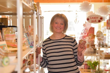 Hobby-Stübchen Lächelnde Frau im Hobby-Stübchen, umgeben von Bastelbedarf und Dekoartikeln in Regalen.