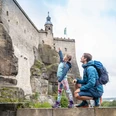 Festung Königstein Familienausflug Festung Königstein: Ein Mann und ein Mädchen in Outdoor-Kleidung betrachten eine große, steinerne Burg; das Mädchen zeigt begeistert nach oben.