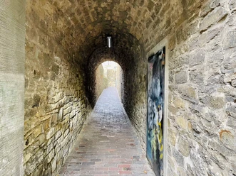 Der Klapperhagen in Osnabrück Geschwungener, historischer Tunnel mit steinernen Wänden und Ziegelboden, beleuchtet und graffiti-dekoriert.