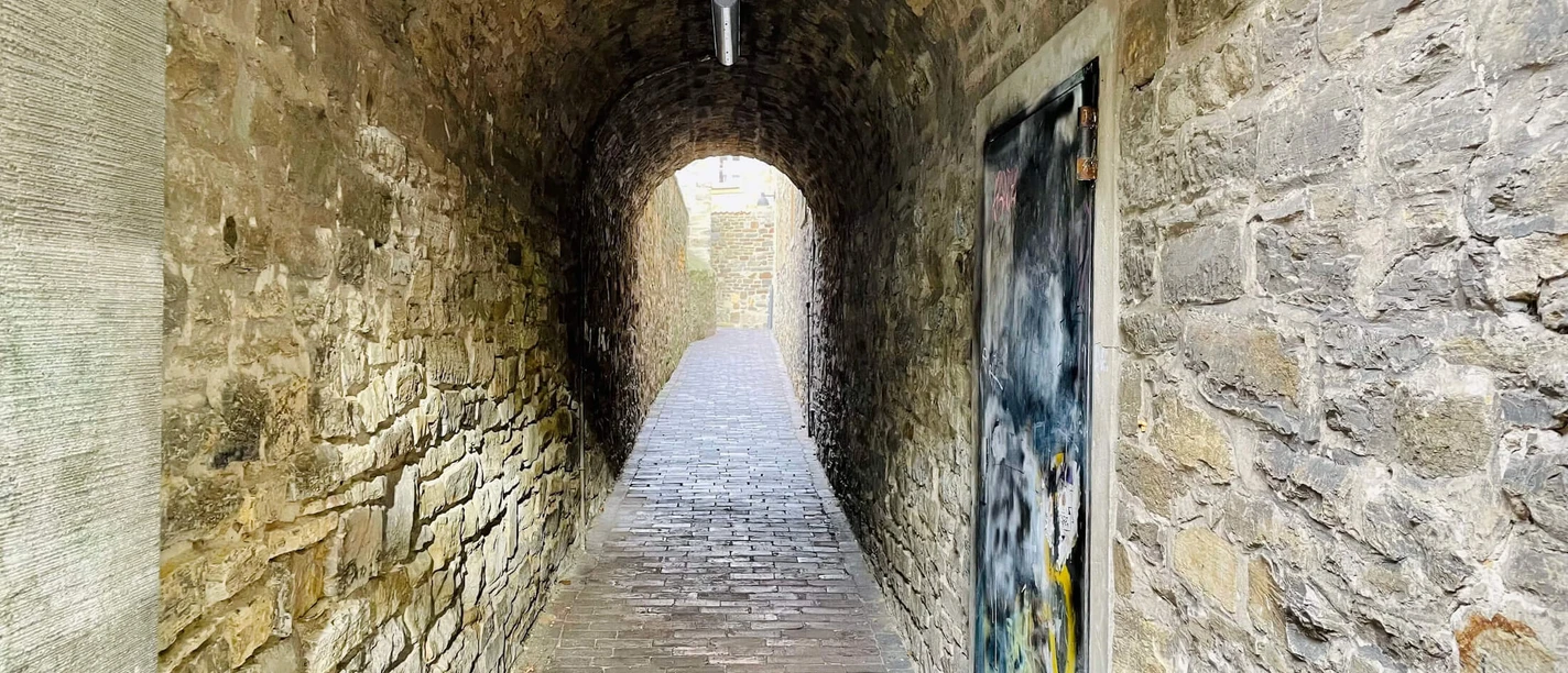 Der Klapperhagen in Osnabrück Geschwungener, historischer Tunnel mit steinernen Wänden und Ziegelboden, beleuchtet und graffiti-dekoriert.