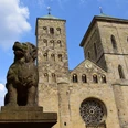 The legendary Löwenpudel in front of St Peter's Cathedral Löwenpudel-Skulptur aus Stein mit zwei Türmen des Osnabrücker Doms und blauem Himmel im Hintergrund.Stone sculpture of a lion poodle with two towers of Osnabrück Cathedral and a blue sky in the background.Stenen sculptuur van een leeuwenpoedel met twee torens van de kathedraal van Osnabrück en een blauwe lucht op de achtergrond.