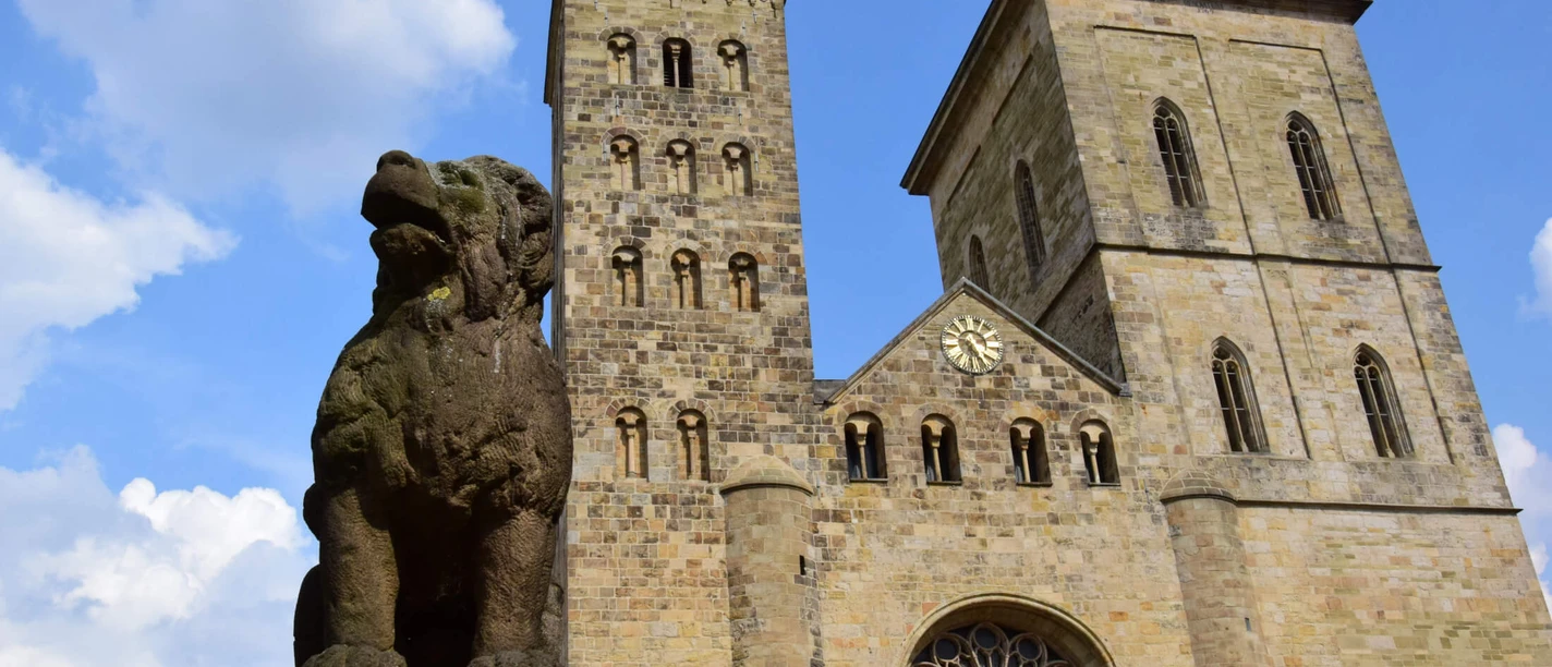 The legendary Löwenpudel in front of St Peter's Cathedral Stone sculpture of a lion poodle with two towers of Osnabrück Cathedral and a blue sky in the background.