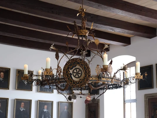 Kronleuchter im Friedenssaal Ein prächtiger Kronleuchter aus Eisen und Bronze mit kunstvollen Verzierungen hängt im Friedenssaal.A magnificent iron and bronze chandelier with ornate decorations hangs in the Peace Hall.En storslået lysekrone af jern og bronze med udsmykkede dekorationer hænger i fredssalen.In de Vredeszaal hangt een prachtige kroonluchter van ijzer en brons met sierlijke decoraties.