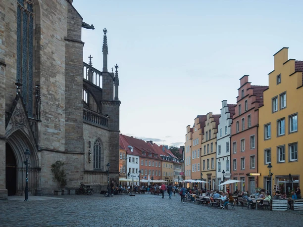 Abendstimmung am Marktplatz Abendliche Marktplatzszene mit beleuchteten Gebäuden und Menschen, die an Tischen im Freien sitzen.