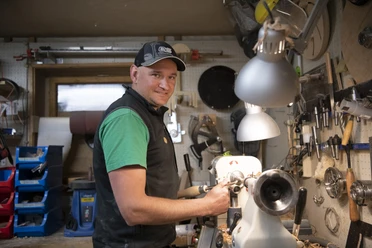 Da Doni Holzstiftmanufaktur Handwerker in einer Werkstatt bearbeitet Holz an einer Drehbank, umgeben von Werkzeugen.